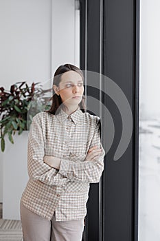 confident business woman stands at window in office looking into distance. thoughtful female