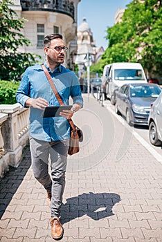 Confident businessman with digital tablet walking on sidewalk during sunny day