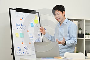 Confident businessman explaining business data on whiteboard during online conference via laptop computer