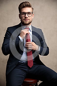 Confident businessman fixing his red tie while wearing glasses