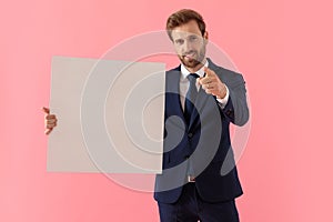 Confident businessman holding a blank billboard and pointing forward