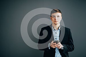 Confident businessman leaning against a wall while using the smartphone on black background