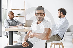 confident businessman looking at camera while colleagues working at table photo