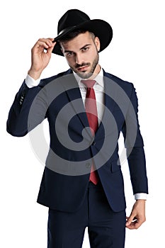 Confident businessman looking forward and fixing his hat