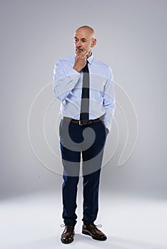 Confident businessman looking thoughtfully and standing against at grey background