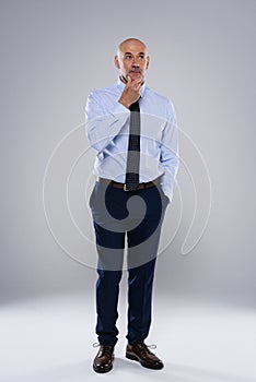 Confident businessman looking thoughtfully and standing against at grey background