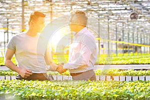 Confident businessman shaking hands with male botanist in greenhouse photo