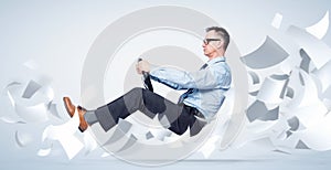 Confident businessman in shirt, tie and glasses flies through sheets of white paper holding a car steering wheel, on background