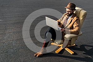 confident businessman sitting in armchair and using laptop