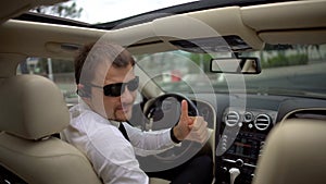 Confident businessman sitting in car, giving thumbs-up gesture, business driver