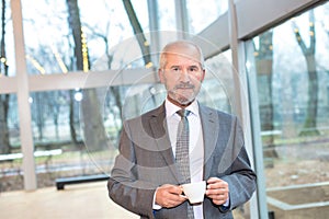 Confident businessman standing while drinking coffee in office