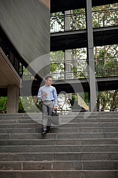 A confident businessman walks down stairs outside a building, holding a coffee cup and a briefcase