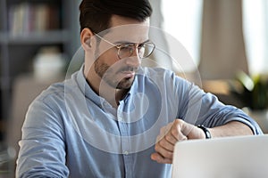 Confident businessman wearing glasses looking at wrist watch, checking time