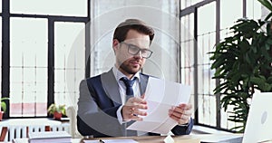 Confident businessman wearing suit reading paper letter sitting at desk