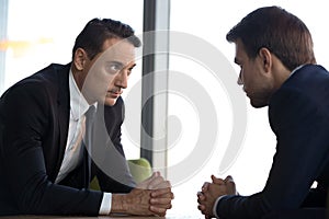Confident businessmen with clasped hands sitting opposite, debate concept