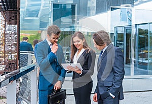 Confident businesspersons talking in front of modern office building. Businessmen and businesswoman have business