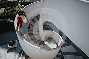 Confident businesswoman descending outdoor spiral staircase in sunlight