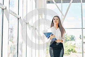 Confident businesswoman going to work holding clipboard in modern office