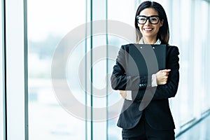 Confident businesswoman going to work holding clipboard in modern office