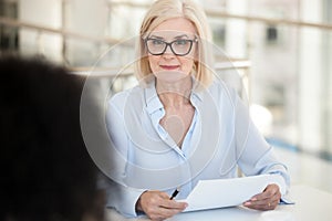 Confident businesswoman hold paper document, listen to colleague at meeting