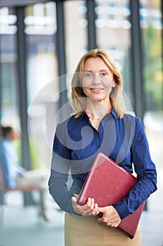 Confident businesswoman holding document while standing against colleagues in office meeting