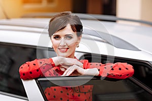 confident businesswoman looking at camera and smiling by open door car. Cheerful successful lady with red lipstick in