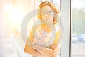 Confident businesswoman standing with arms crossed at new office with yellow lens flare in background