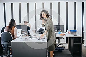 Confident businesswoman talking on phone in modern office with colleagues working in background