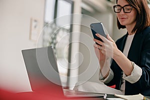 A confident businesswoman is using a smartphone and laptop in a modern office setting photo