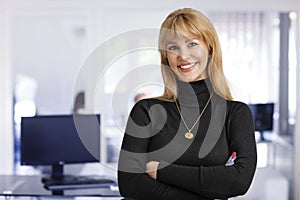 Confident businesswoman wearing black sweater and standing in the office with folded arms