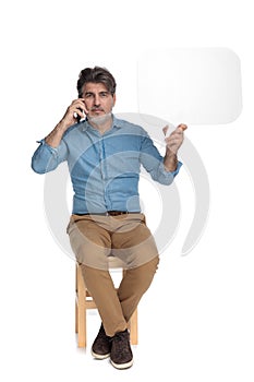 Confident casual man talking on phone and holding speech bubble