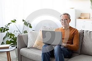 Confident casual mature man using laptop at home