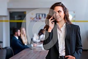 Confident caucasian blonde businesswoman talks on smartphone in modern office, standing with hand in pocket. Female