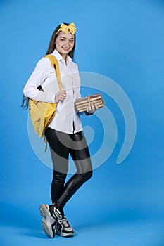 Confident caucasian female student with backpack posing, while standing with crossed legs in studio.