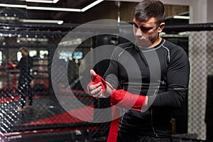 Confident Caucasian Male Kickboxer Fighter Preparing For Fight, Wrapping Hand In Red Bandage