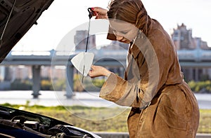 Confident caucasian woman driver checking oil level in car engine dipstick