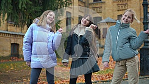 Confident charming positive schoolgirls dancing simultaneously standing outdoors on autumn day. Front view portrait of