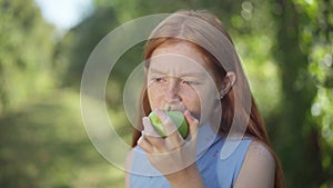 Confident charming redhead teenage girl biting chewing healthful apple smiling looking at camera. Portrait of happy