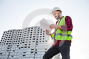 Confident construction engineer in hardhat with using cell phone on construction