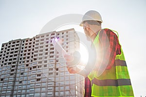 Confident construction engineer in hardhat with using cell phone on construction