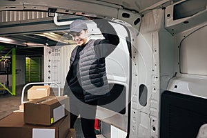 Confident courier leaning on van looking on cardboard boxes