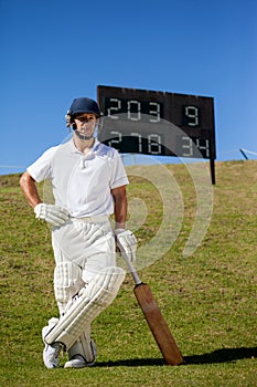 Confident cricket player with bat standing against scoreboard