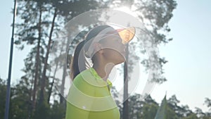 Confident cute girl in a sportswear holds a tennis racket while standing on the tennis court oudddoors. Young tennis