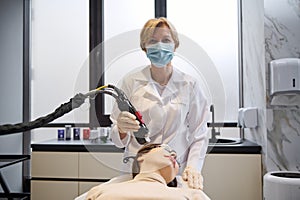 Confident dermatologist doctor performs cosmetic procedures on a woman`s face using a modal laser to remove age and age spots