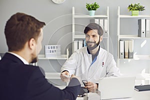 Confident doctor gives the patient a prescription while sitting at a table in a clinic office.