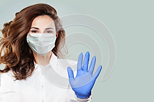 Confident doctor or nurse wearing a medical face mask showing stop pandemic gesture. Woman in safety mask and medical gloves.