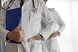 Confident doctors with hands in pockets against white background