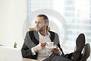 Confident dreamy businessman relaxing with cup of coffee at work