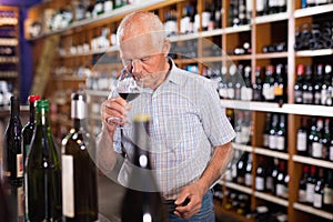 Confident elderly man tasting red wine in wine store before buying