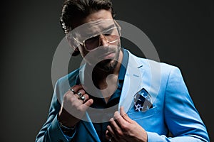 confident elegant businessman with glasses adjusting blue suit and looking away